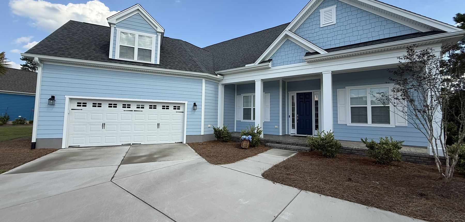 Light blue two-story coastal home with white trim, a white garage door, and a clean concrete driveway.