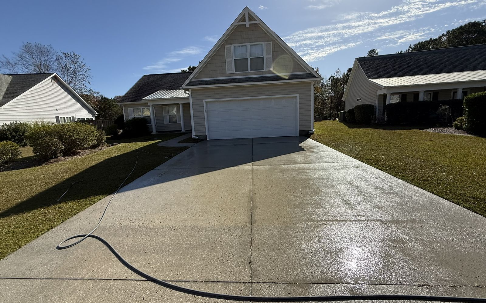 Tan home with a front-facing gable and a freshly washed concrete driveway on a sunny day.